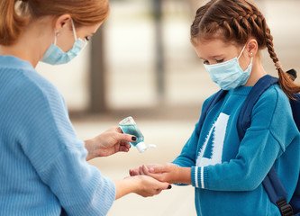 Concept of preventing a coronavirus covid-19 and viral infections. Mother treats her child's hands with a sanitizer before school.