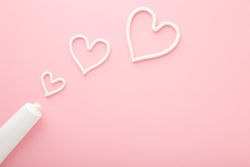 Heart shapes created from cream. White tube on light pink table background. Pastel color. Care...