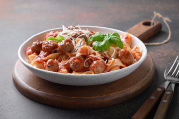 Pasta fettuccine with meatballs, parmesan, tomatoes, basil on brown. Close up.