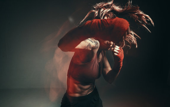 Cool female fighter in boxing bandages trains in studio in neon light. Mixed martial arts poster. Long exposure shot