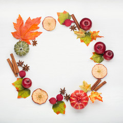 Wreath of dry maple leaves, flowers and apple. White table background.