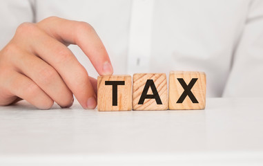 Close up young man's hand in white shirt wooden block cube for tax wording on white marble table floor