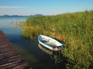 White wooden boat next to the reeds and beach expiring at the southern shore of the lake Balaton,...