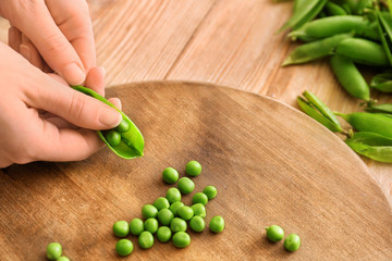 Woman preparing fresh peas on table, closeup