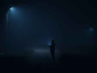 Night city in a thick wet fog . Silhouette of a man with a flashlight walking along the road at night. Mystical dark landscape. film toning,