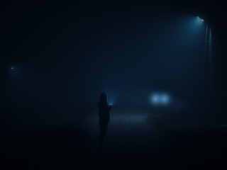 Night city in a thick wet fog . Silhouette of a man with a flashlight walking along the road at...