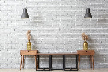Wooden stand with decor and lamps near grey brick wall in room