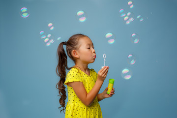 Asian girl playing with soap bubbles in the Studio on a blue background