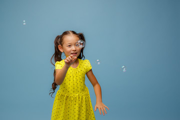 Asian girl playing with soap bubbles in the Studio on a blue background