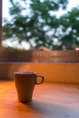 Taza de cafe saliendo humo frente a una ventana en una mesa d emadera