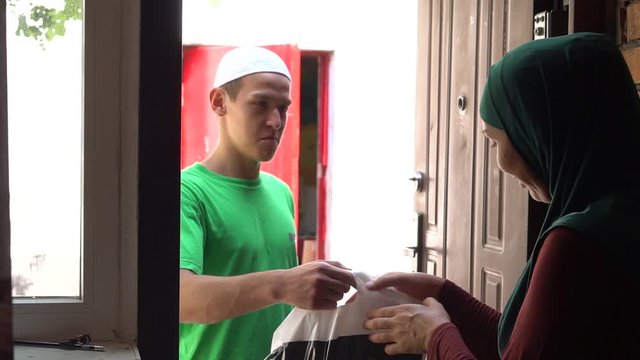 A young Muslim volunteer gives a bag of food to a needy Islamic refugee family. Charity, festive meals, gift-giving, donation. Food for the poor, feeding the hungry, charity organization