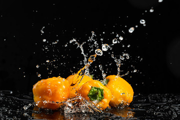 Fototapeta na wymiar Sweet peppers on a black background with drops and splashes of water