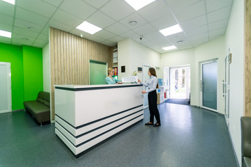 Full length portrait of female patient conversing with nurse at reception desk in hospital.