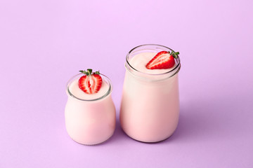 Jars of strawberry yogurt on color background