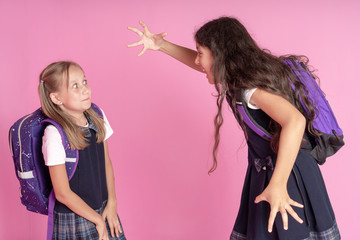 Two schoolgirls in school uniforms are fighting on a pink background