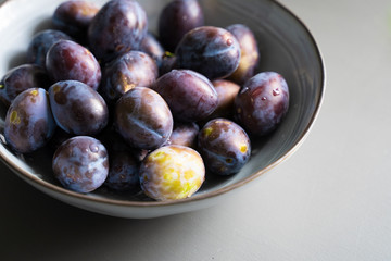 fresh plum fruits in grey bowl on table