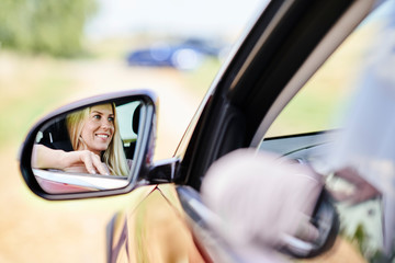 Fototapeta na wymiar Reflection in wing mirror of smiling woman driving car