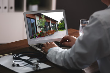 Real estate agency online service. Doctor choosing new house via laptop, closeup