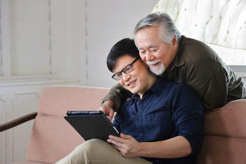 Senior Asian man in retirement age looking at photo of product available online in his son digital tablet with copy space 