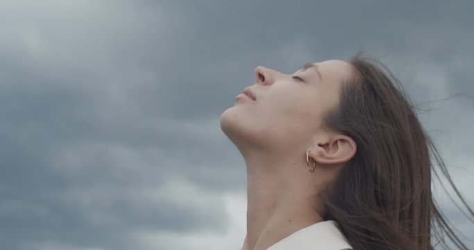 Low angle portrait of woman enjoying fresh air nature life outdoors on cloudy sky background. Beautiful girls face without make up turned up slow motion handheld device. Happiness calmness