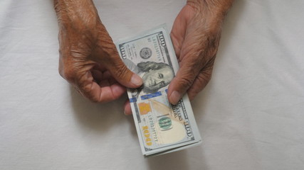 Wrinkled female hands holds cash and counts foreign currency over the table. Arms of elderly grandmother puts one hundred dollar banknotes on the desk. Money concept. Top view Slow motion