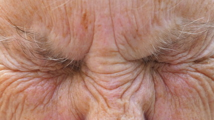 Portrait of mature grandmother looks into camera with amazed facial expression. Close up of elder grandma strongly screws up her gray eyes. Wrinkled mature female face shows surprise emotions