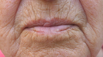 Close up lips of mature grandmother. Mouth of elder grandma sends air kiss into camera. Senior woman with wrinkled skin does kissing gesture. Slow motion