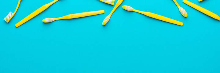 Top view photo of many new yellow toothbrushes over turquoise blue background with copy space. Flat lay image of manual plastic toothbrushes with right side composition.