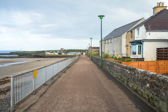 Deserted paved pathway along a beach with houses on the right side on a cloudy summer day