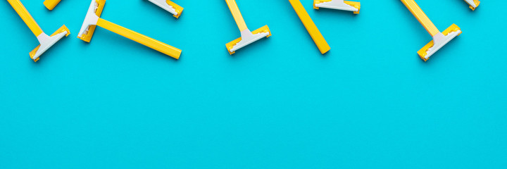 Many disposable unisex razors on the turquoise blue background. Top view of yellow plastic razors...