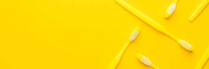 many new plastic yellow toothbrushes in order on the yellow background with copy space