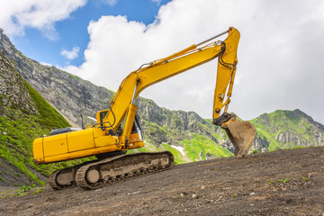 Excavator heavy equipment in mountains on steep range slopes.