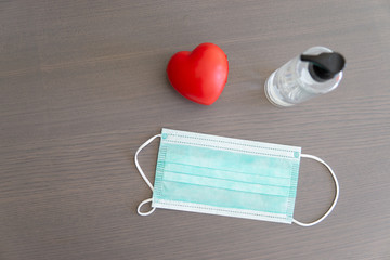 Mascarilla quirúrgica junto a corazón y gel sobre un fondo de madera gris