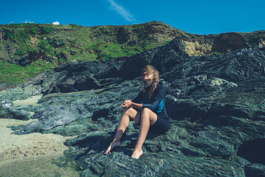Young woman in wetsuit sitting on rocks by the sea in summer