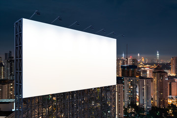 Obraz premium Blank white road billboard with KL cityscape background at night time. Street advertising poster, mock up, 3D rendering. Side view. The concept of marketing communication to promote or sell idea.