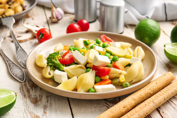 Plate with tasty conchiglie pasta and vegetables on table