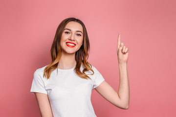 Fototapeta premium Caucasian woman in white t-shirt with red lips smiling and showing thumb up isolated on pink background