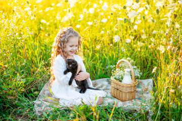 little beautiful girl sitting on the lawn in summer with a black kitten, picnic in nature