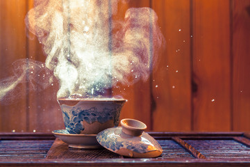 Traditional chinese painted clay tea brewing cup with cloud of steam and splashing hot water on...
