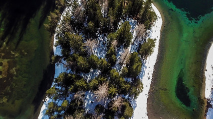 A top down drone shot of Green Lake in Austrian Alps. The lake shimmers with many shades of green and turquoise. Thick forest around it. Winter in the mountains. There is snow on the ground. Wandering