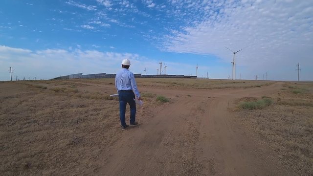 An engineer in a hard hat looks at a project at a new type of power plant, wind turbines and solar panels. The project does not correspond to reality, the engineer gets upset and abandons the project.