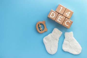 14 DECEMBER text on wood cubes, pair of cute knitted baby socks and wooden teether bear on blue background. Date of child birth. Newborn concept. Flat lay, top view with copy space.