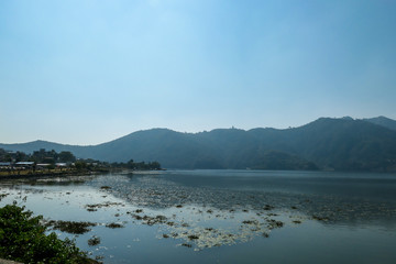 A view on Phewa Lake in Pokhara, Nepal. There are high Himalayan ranges around the lake. Calm surface of the lake. Clear and sunny day. Undisturbed peace. Serenity and relaxation.
