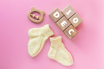 10 DECEMBER text on wood cubes, pair of cute knitted baby socks and wooden teether bear on pink...