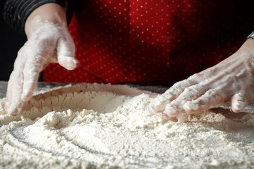 Flour on a wooden table surrounded by female hands with free space for an advertising product