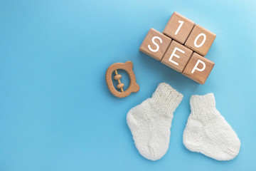 10 SEPTEMBER text on wood cubes, pair of cute knitted baby socks and wooden teether bear on blue background. Date of child birth. Newborn concept. Flat lay, top view with copy space.
