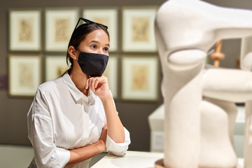 Woman visitor wearing an antivirus mask in the historical museum looking at pictures.