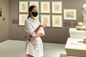 Woman visitor wearing an antivirus mask in the historical museum looking at pictures.