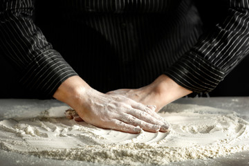 Fototapeta premium Flour on a wooden table surrounded by female hands with free space for an advertising product