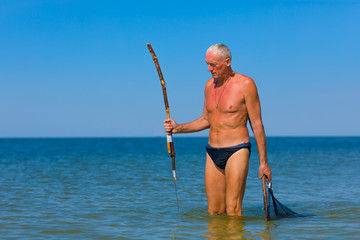 Man with a homemade spear looks out for prey in the sea.